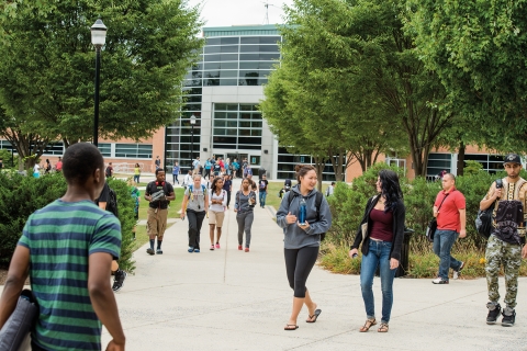 A wide shot of several groups of students walking and talking on a campus walkway